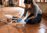 Woman kneeling on terracotta floor applying sealant with brush wearing gloves